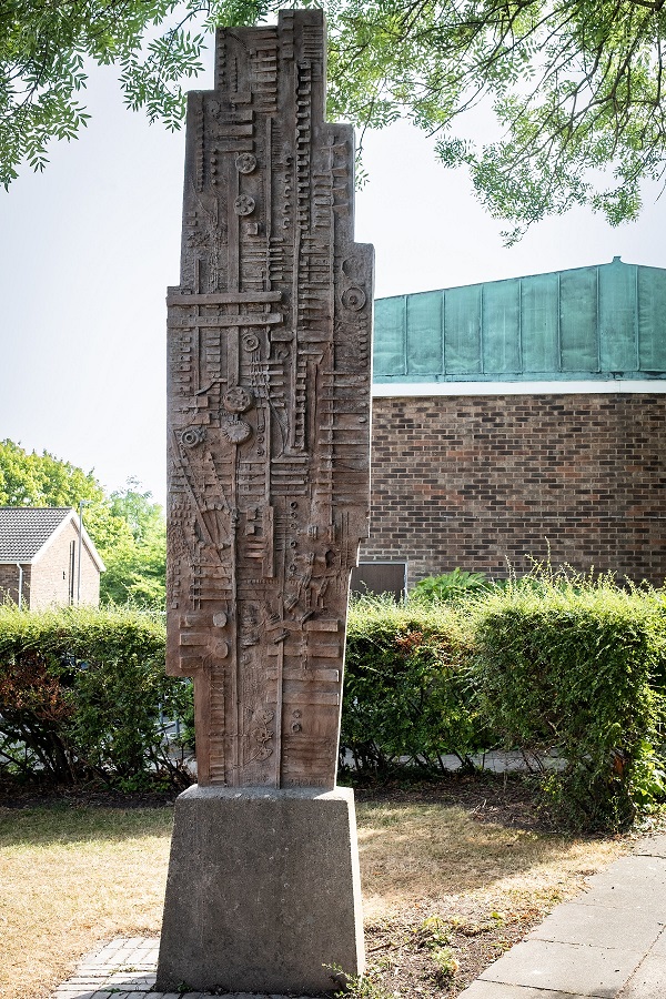 Tall sculpture in browny red concrete with relief design.